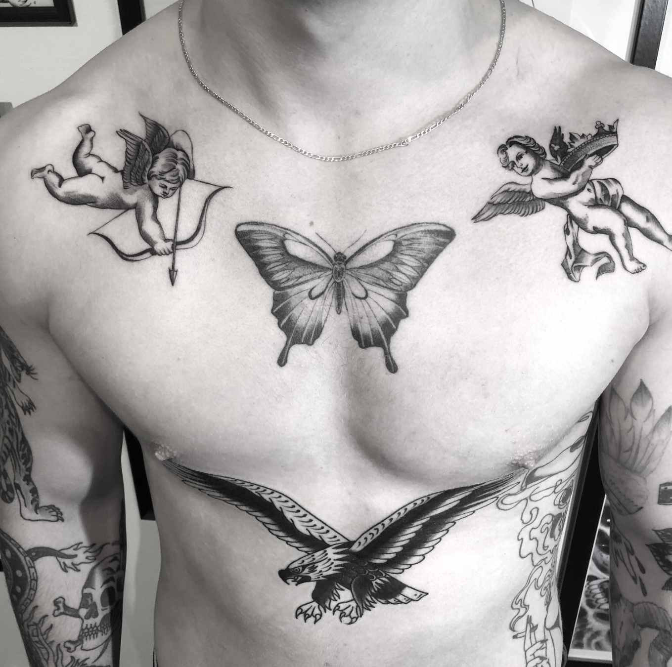 Black-and-white torso with butterfly and angel tattoos, including a large butterfly on the chest and eagle tattoo below.