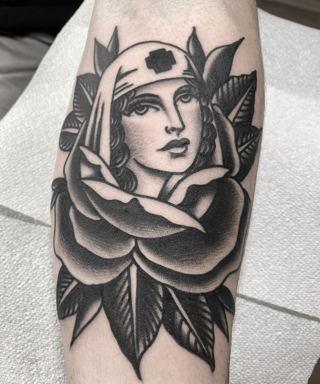 Black-and-gray tattoo of a woman’s face framed by a rose and leaves on a forearm