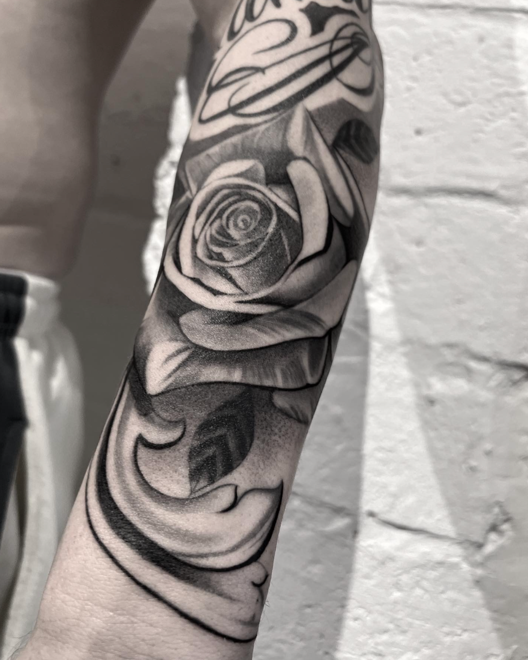 Black-and-gray floral tattoo sleeve on a forearm, featuring a rose and swirling abstract shading.