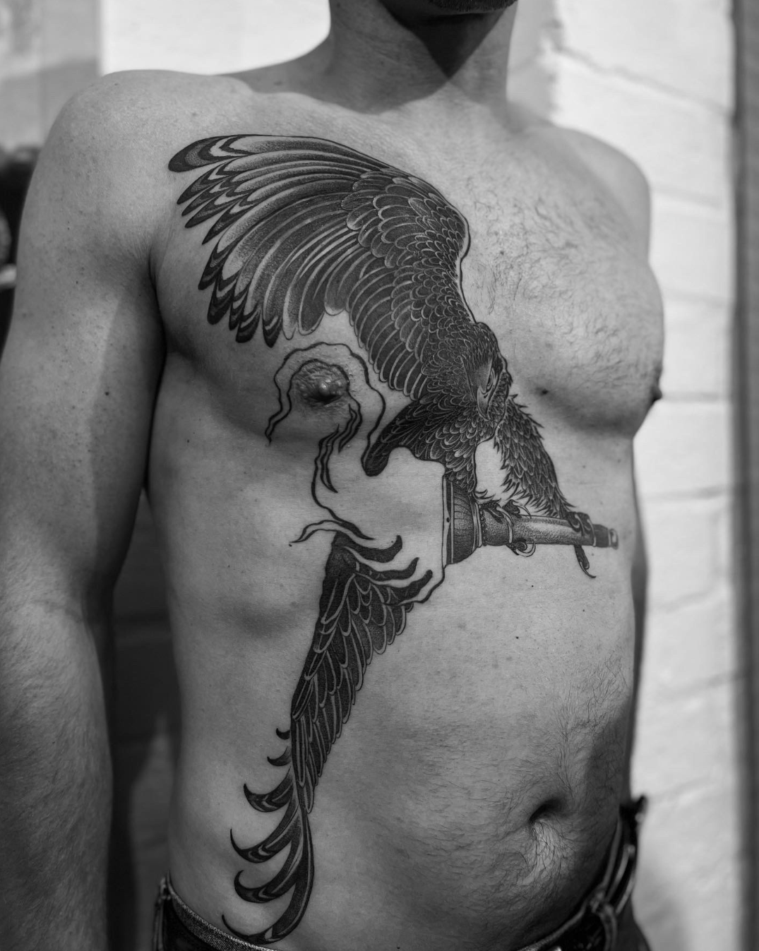 Black-and-white torso with a large bird tattoo on the side of the chest and abdomen