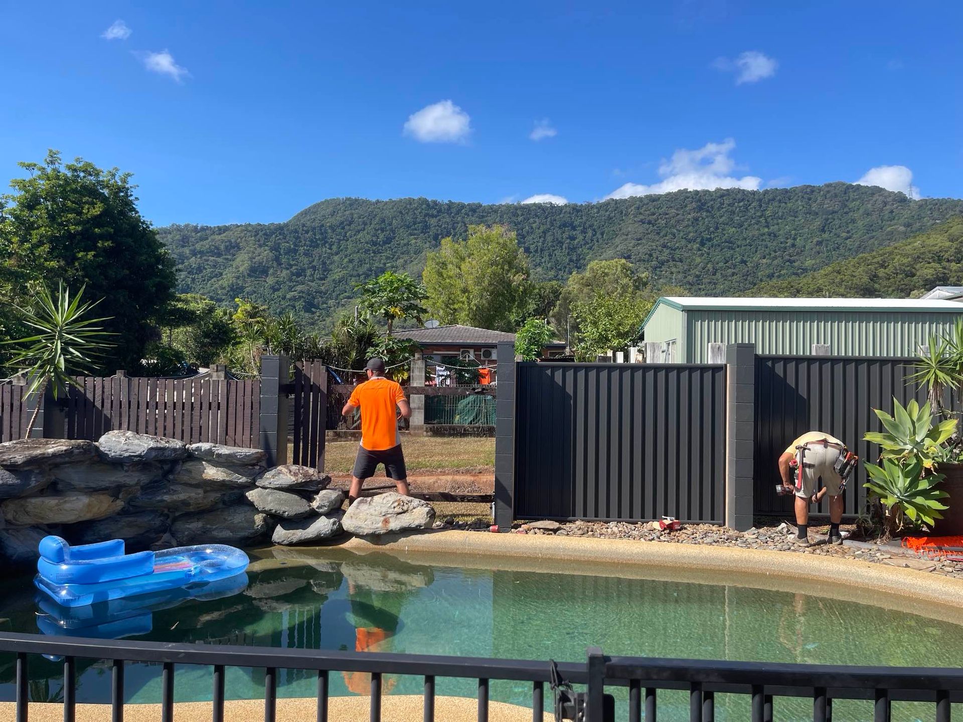 Two men are working on a fence around a swimming pool.