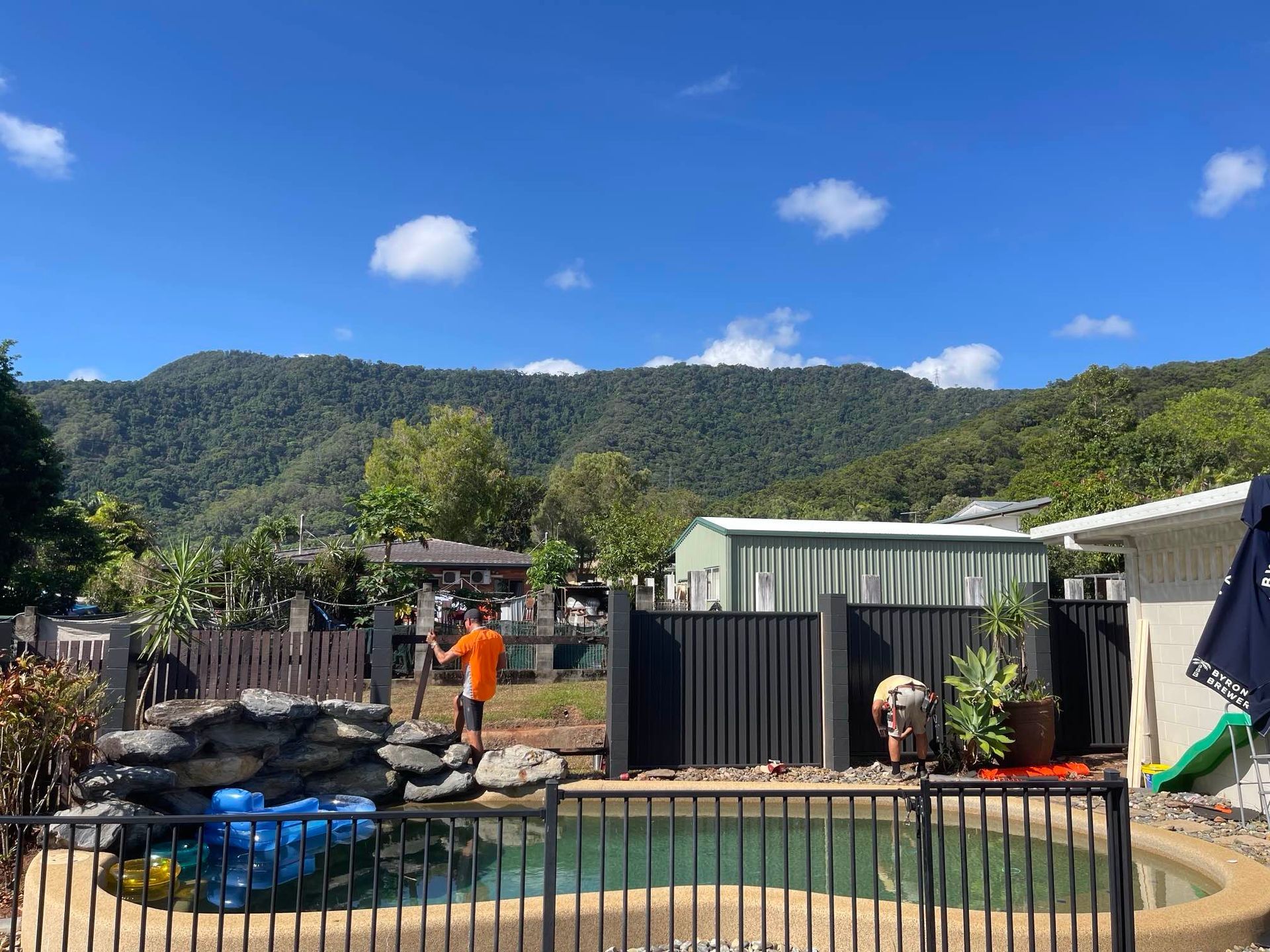 A man is standing next to a pool with mountains in the background — Slim Fox Home Improvements in Mooroobool, QLD