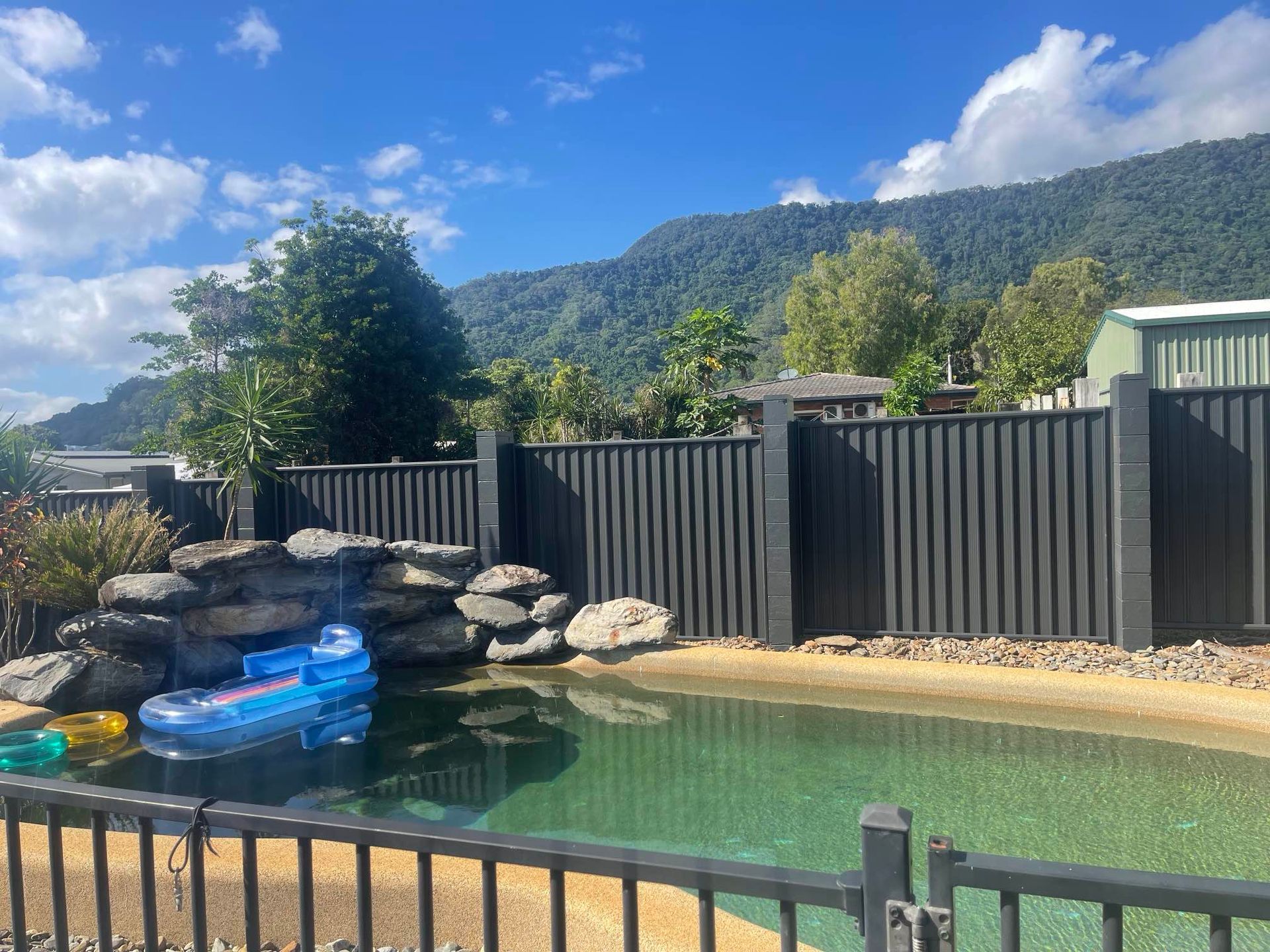 A fence surrounds a swimming pool with mountains in the background — Slim Fox Home Improvements in Mooroobool, QLD