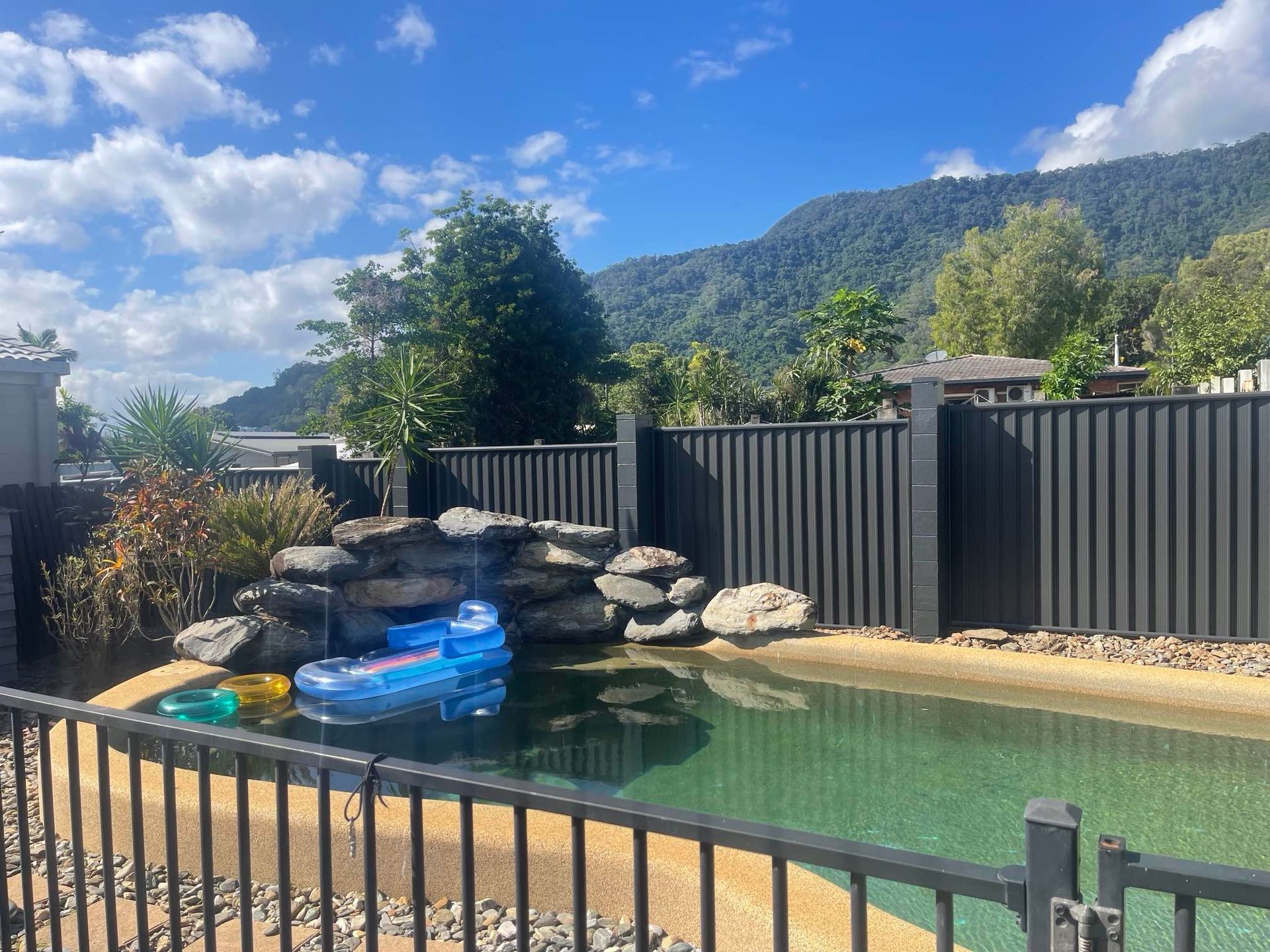 A fence surrounds a swimming pool with a waterfall in the background — Slim Fox Home Improvements in Mooroobool, QLD
