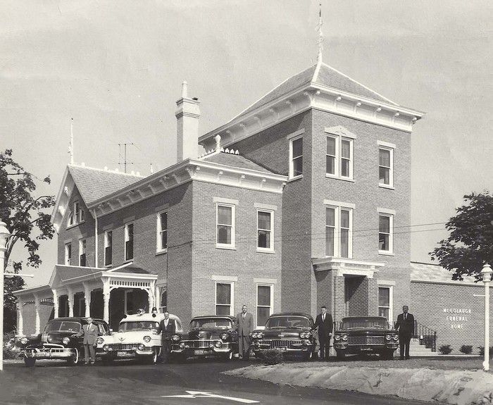 Historic brick building with parked vintage cars out front, seen in black and white.