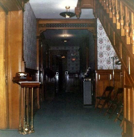 Dim hallway with wood paneling, staircase, floral wallpaper, and a dark doorway at the end