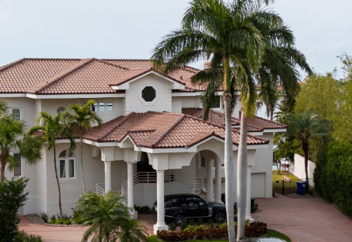 Large white stucco house with red tile roof and palm trees in the front yard
