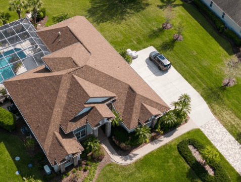 Aerial view of a tan-roofed house with a driveway, car, and green lawn.