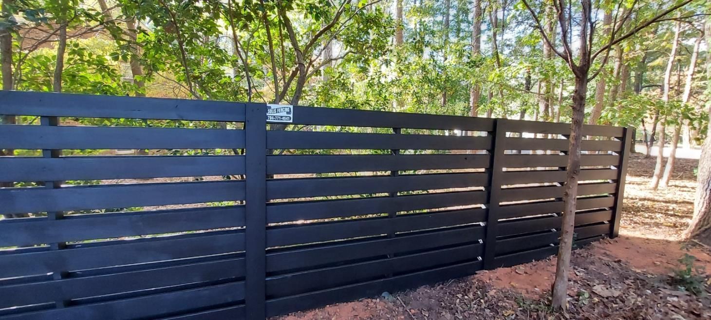 A black wooden fence is surrounded by trees in a forest.