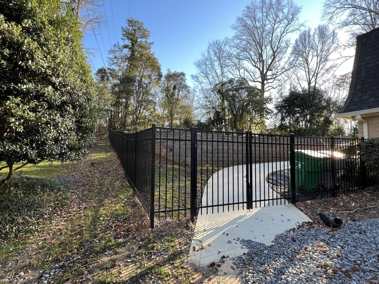 A black fence surrounds a driveway in a backyard.