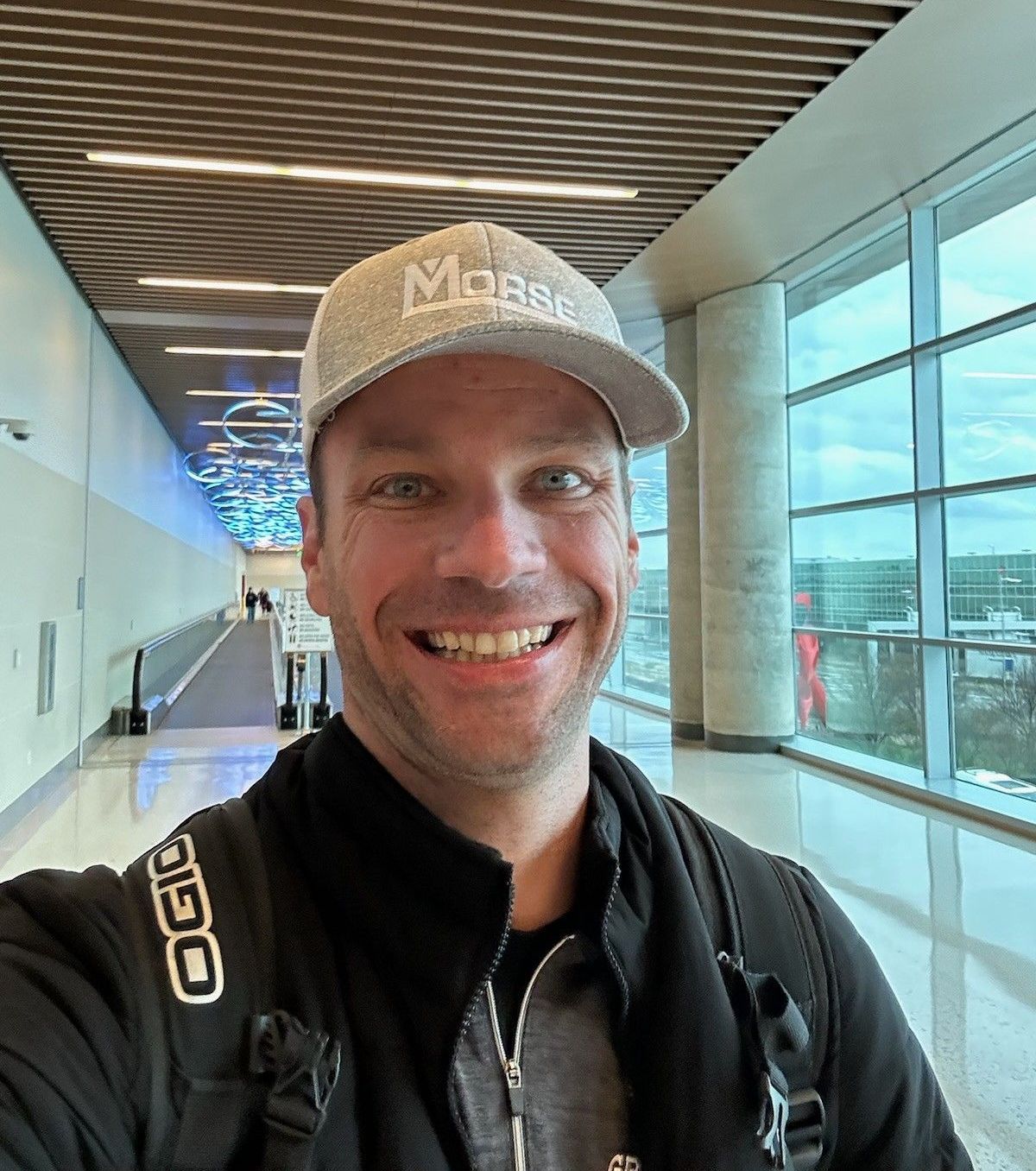 A man wearing a hat and a backpack is taking a selfie in an airport.