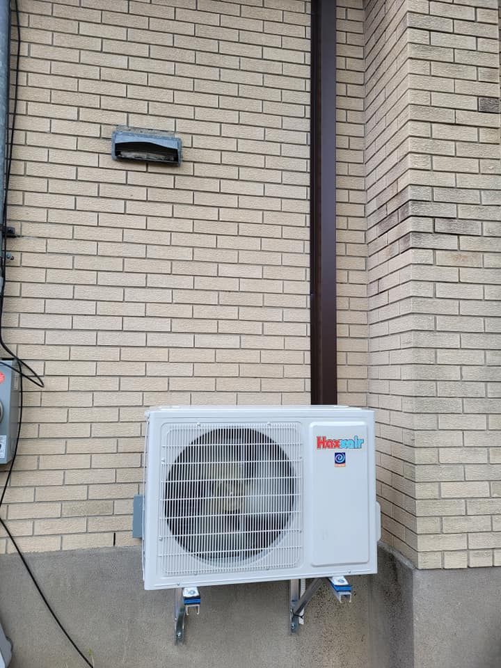 Unité de climatisation fixée sur un mur en briques, avec une sortie d'air et un tuyau.