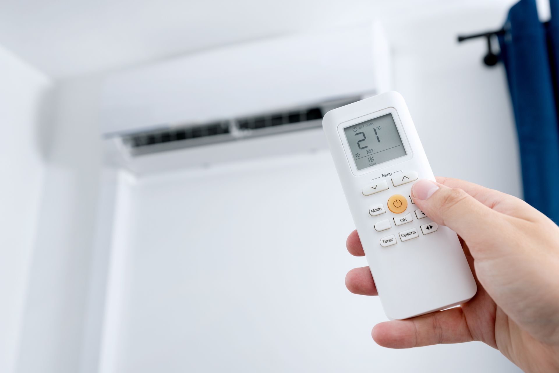 Main tenant la télécommande du climatiseur, la pointant vers l'unité murale, température réglée sur 21.