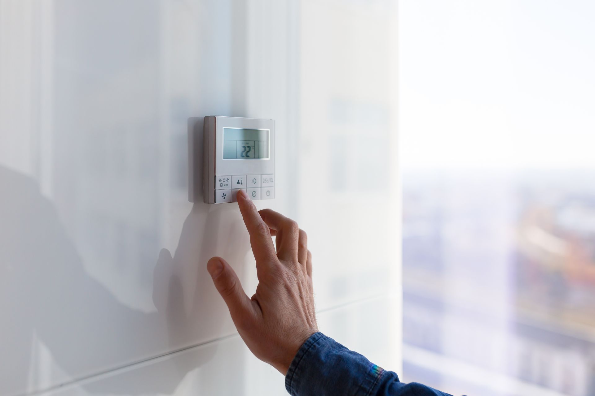 Thermostat à réglage manuel sur un mur blanc. L'affichage est visible, avec un paysage urbain en arrière-plan.
