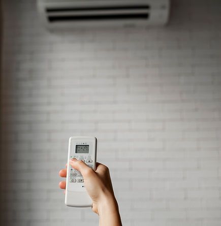 Main tenant une télécommande de climatiseur, pointant vers un appareil blanc fixé au mur.
