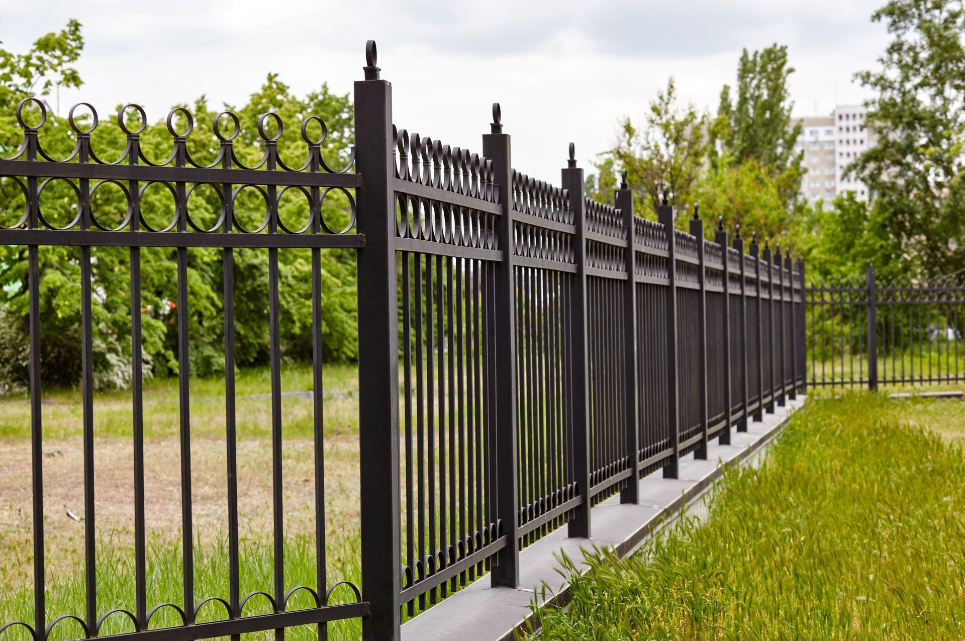 Black metal fence along a grassy path with trees in the background