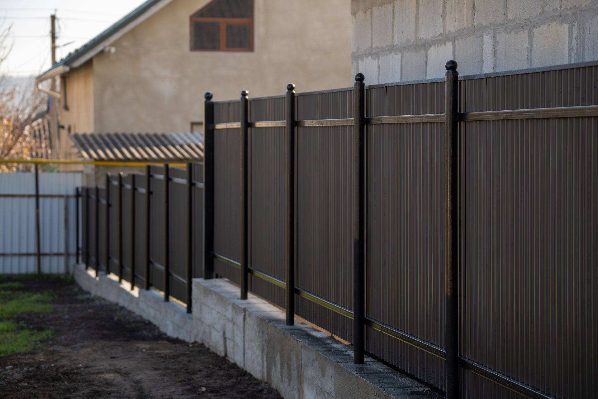 Black metal fence along a concrete wall beside a house and dirt path