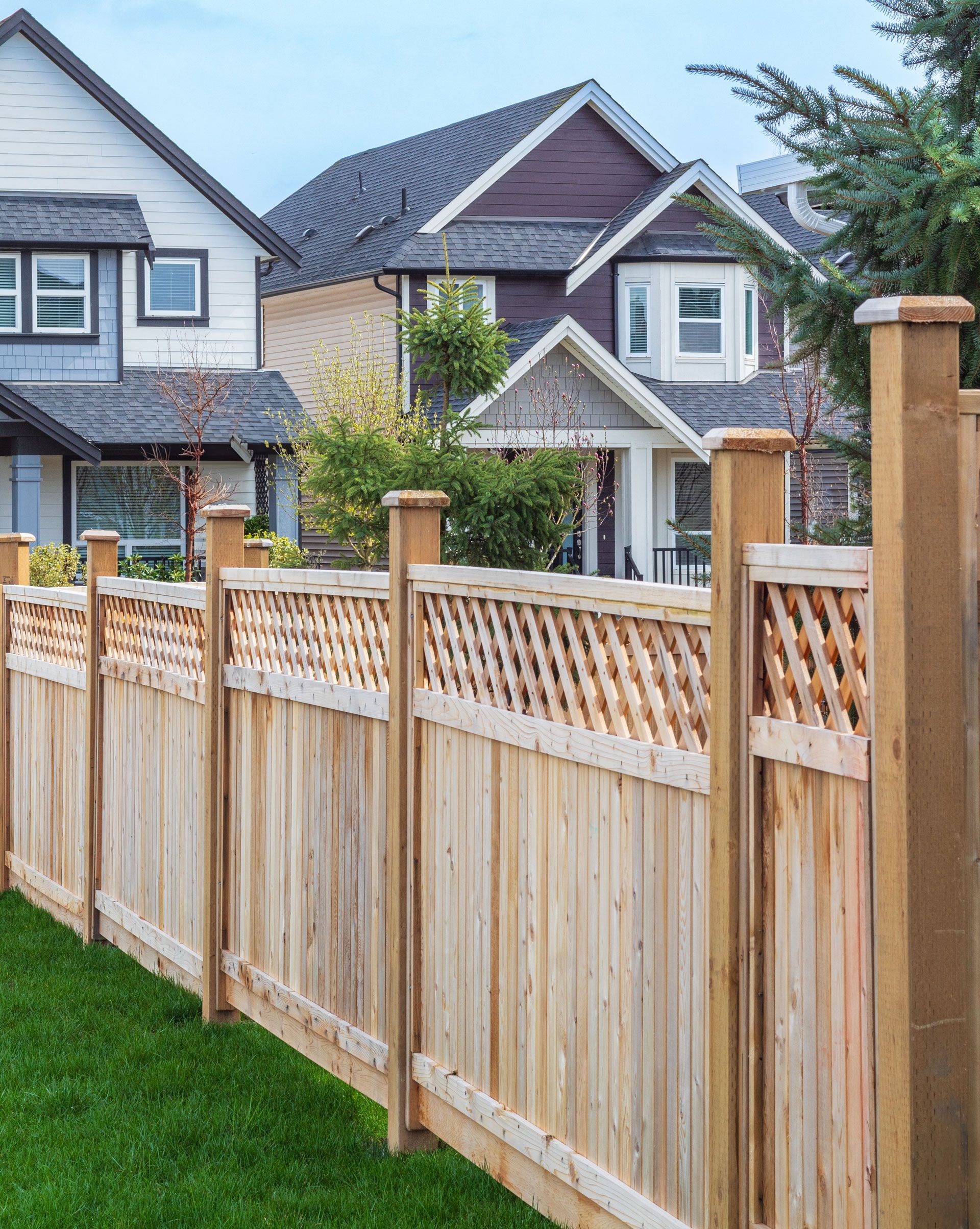 Wooden backyard fence in front of a house with a green lawn and white trim.