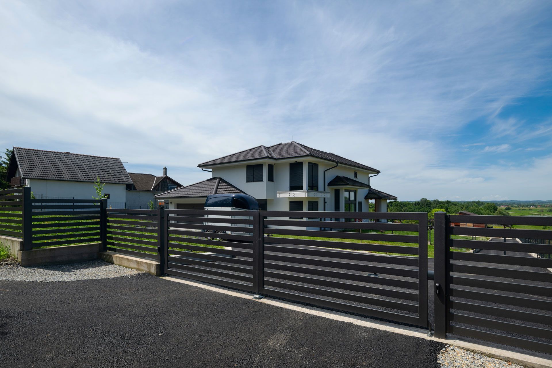Modern house behind a dark metal fence under a bright blue sky