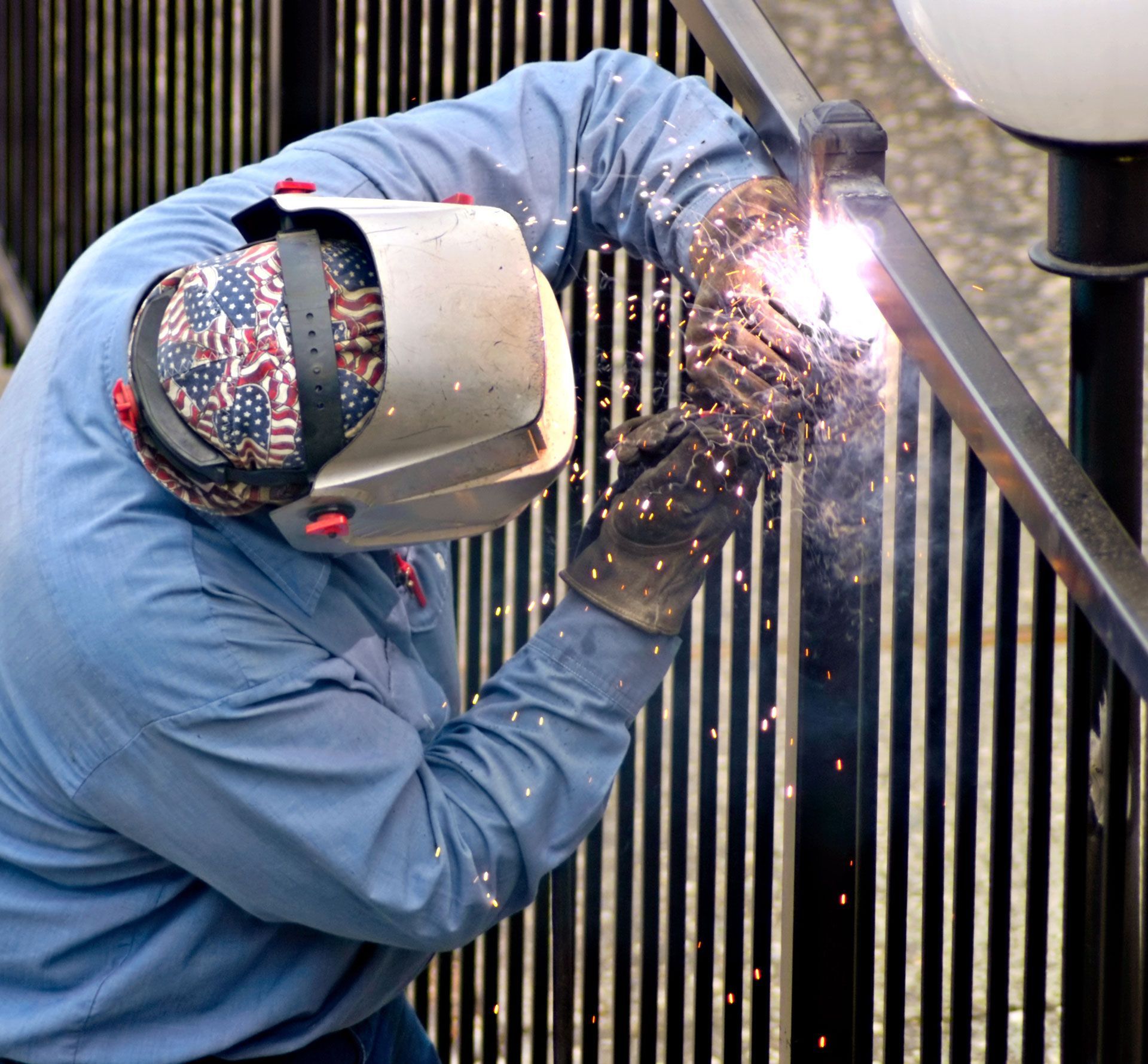 Welder in blue protective gear sparks metal while working on a steel structure outdoors