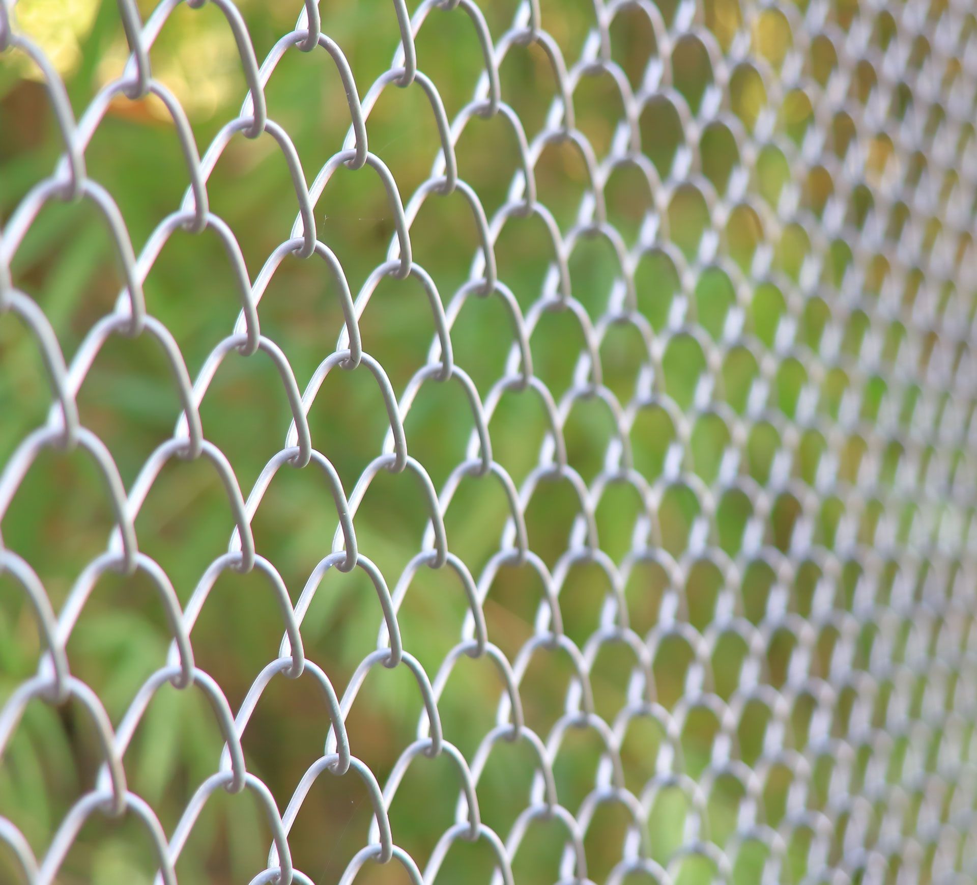 Close-up of silver chain-link fence with blurred green background