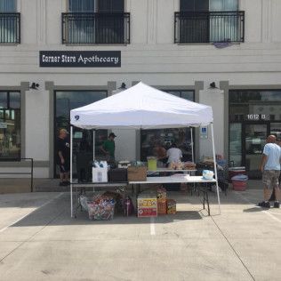 A white tent set up in front of a store, with tables displaying items for sale and people nearby.