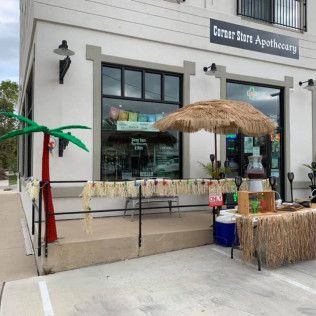 Exterior of a pharmacy, Corner State Apothecary, with a tiki-themed display and refreshments outside.