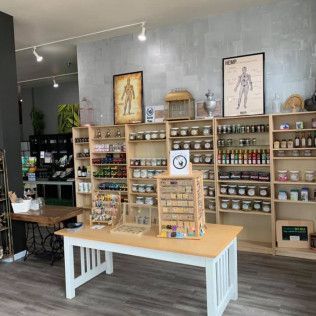 Inside a shop; shelves of jars and bottles; display table with jewelry; anatomy posters on wall.