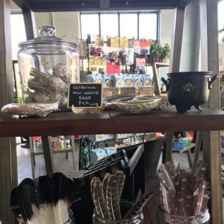 Shelf display with sage, feathers, a cauldron, and other spiritual items in a shop.