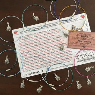 Jewelry display: silver necklaces with leaf pendants, surrounding a business card and list of shops.