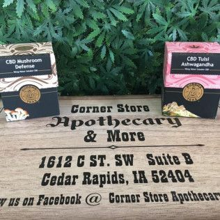Two boxes of CBD products from Corner Store Apothecary, Cedar Rapids, IA, with green foliage background.