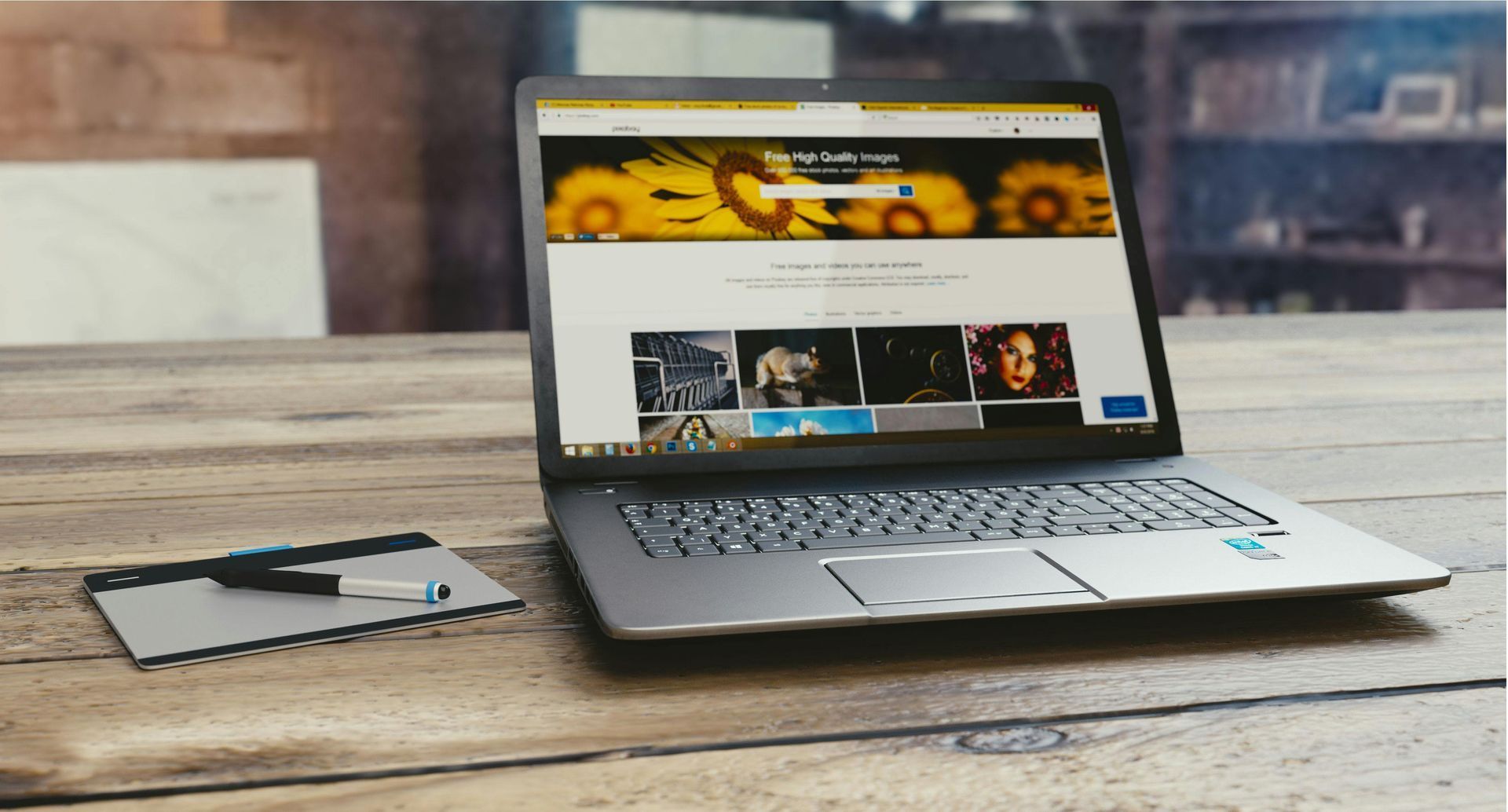 Laptop displaying website with images on a wooden desk, next to a tablet.
