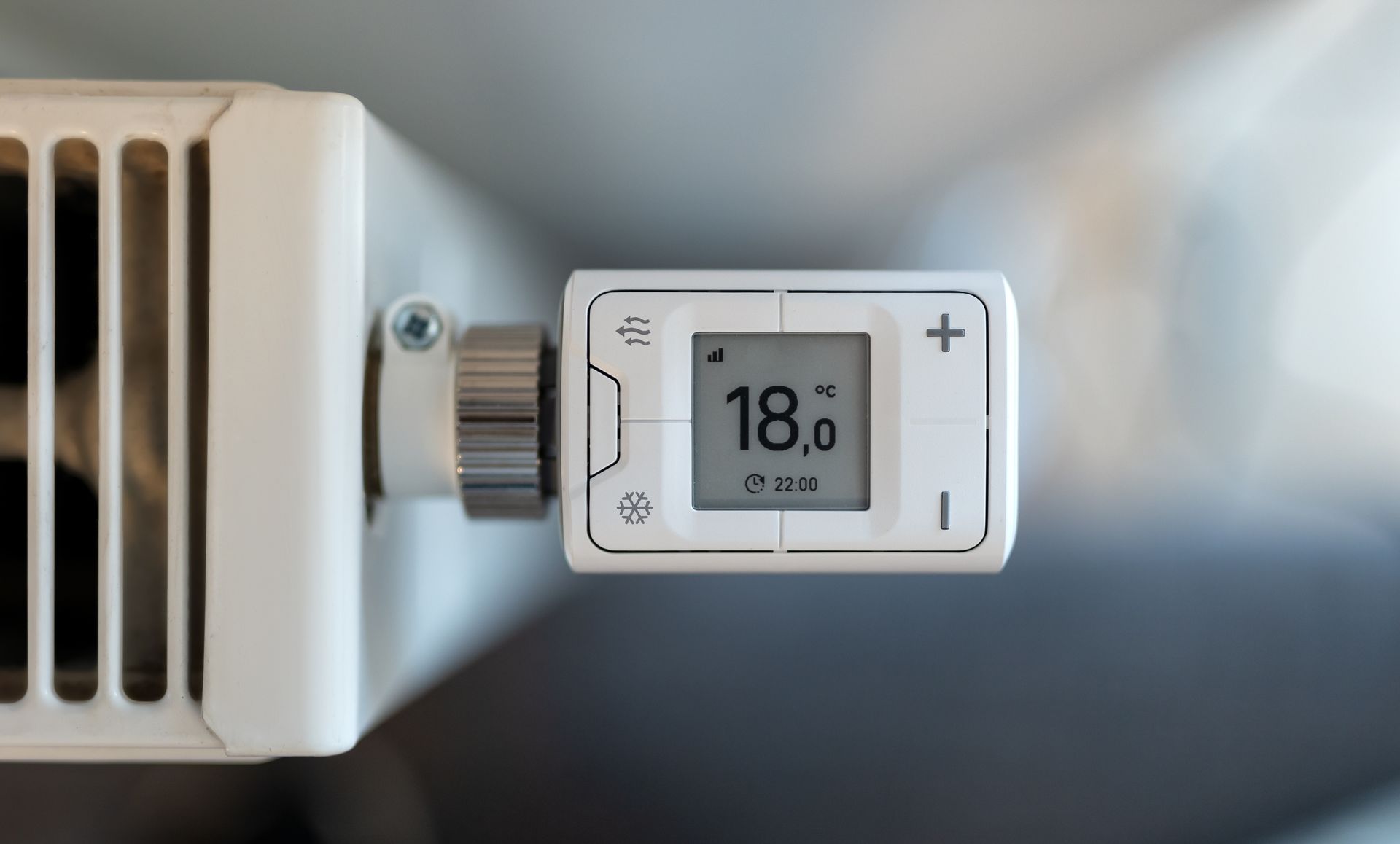 Thermostat showing 18.0°C mounted beside a radiator in a white room.