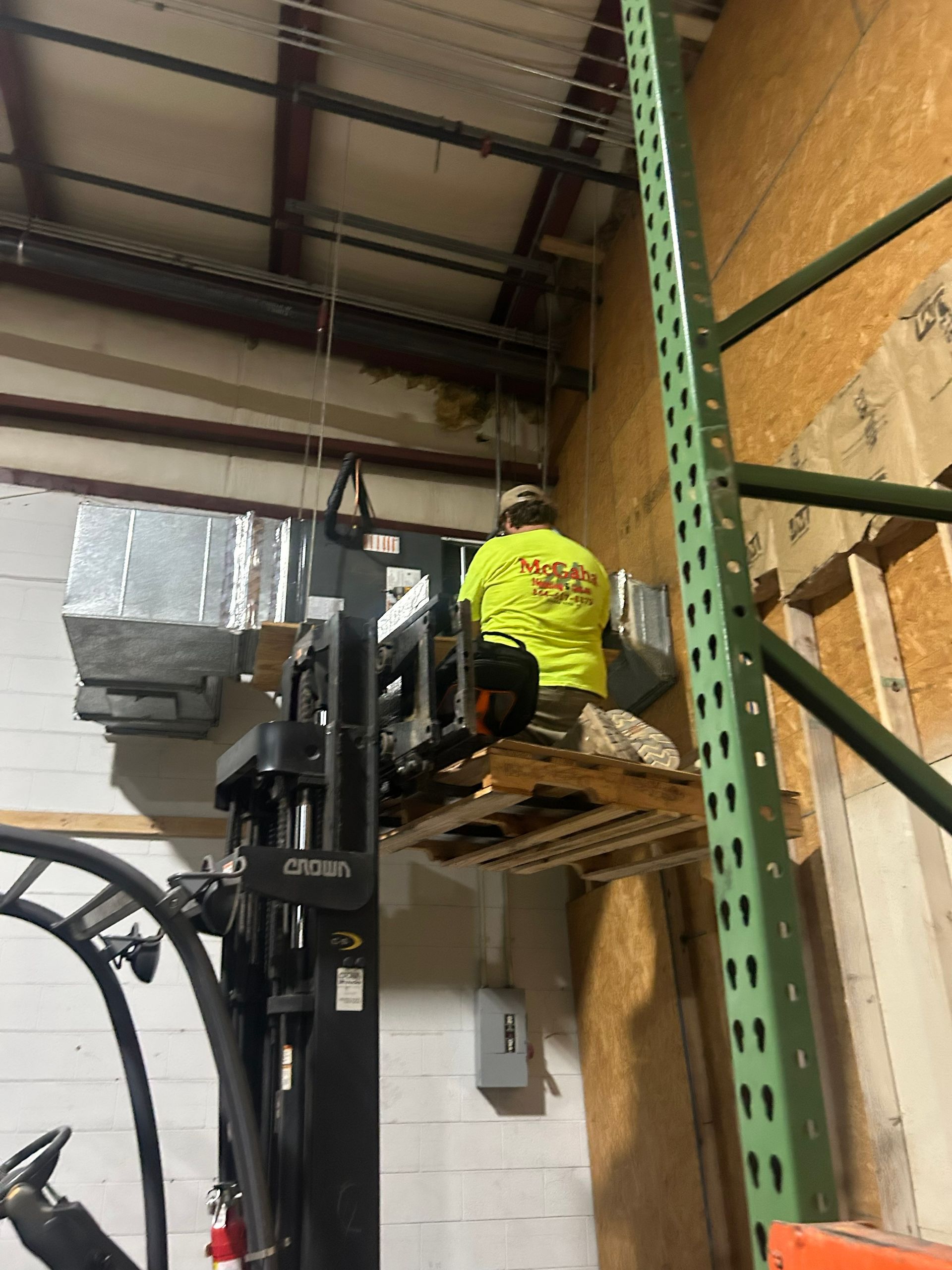 Worker on a forklift platform installing items on a warehouse shelf.