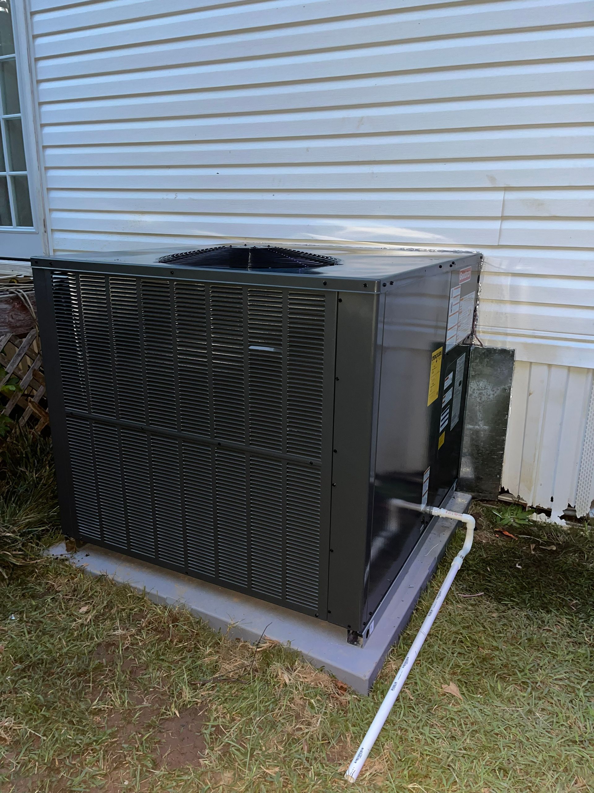 Outdoor central air conditioner unit beside a house with black grille and white siding backdrop