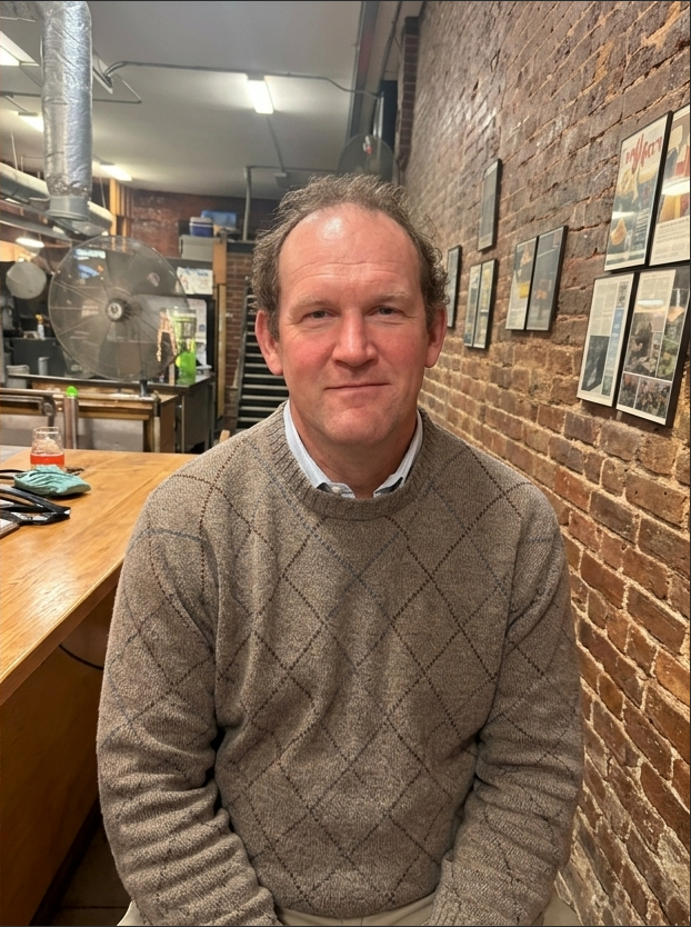 Co-Founder David S. smiling in a suit jacket and striped shirt on a dark background