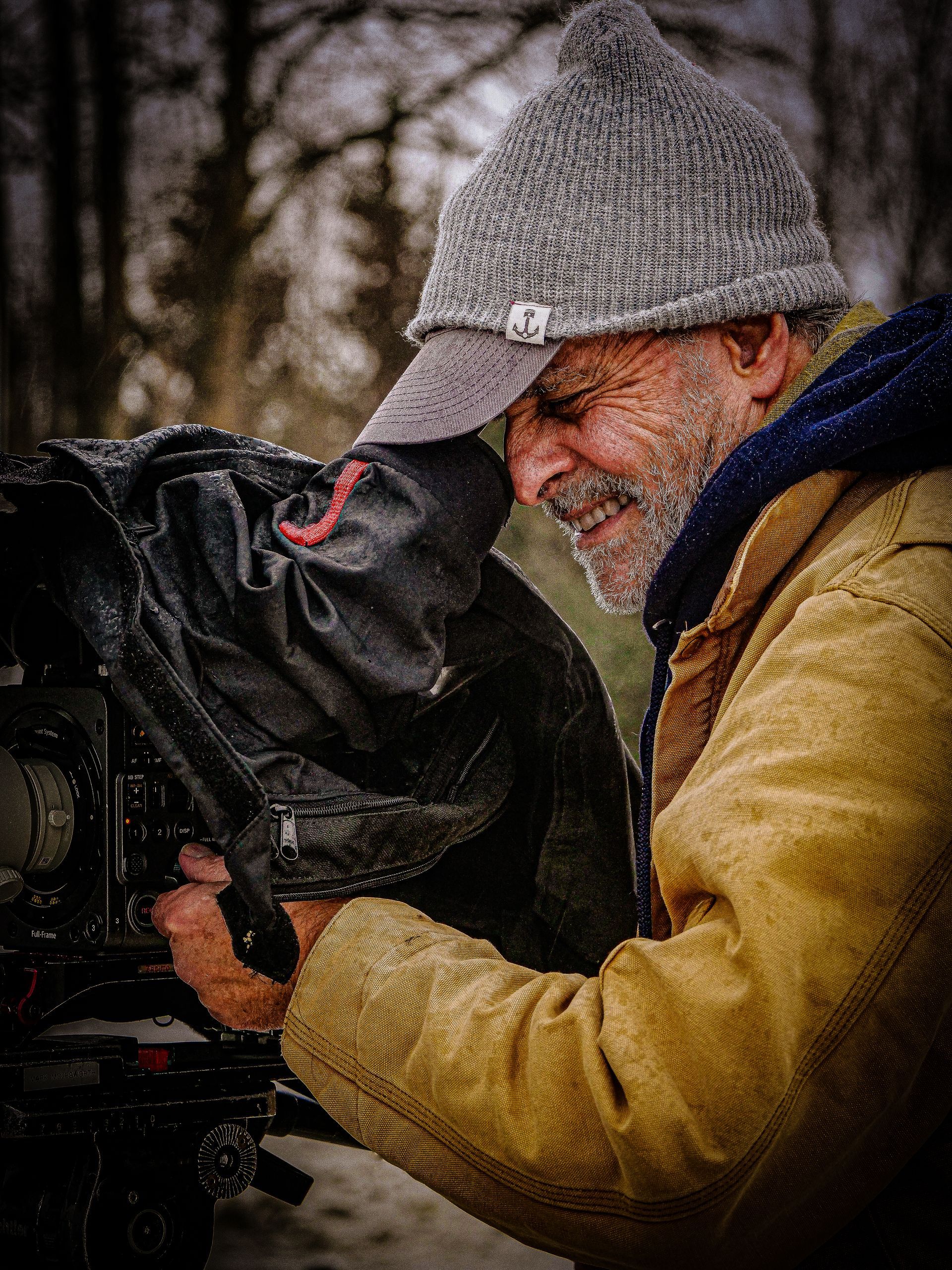 A man wearing a hat and a jacket is holding a camera.