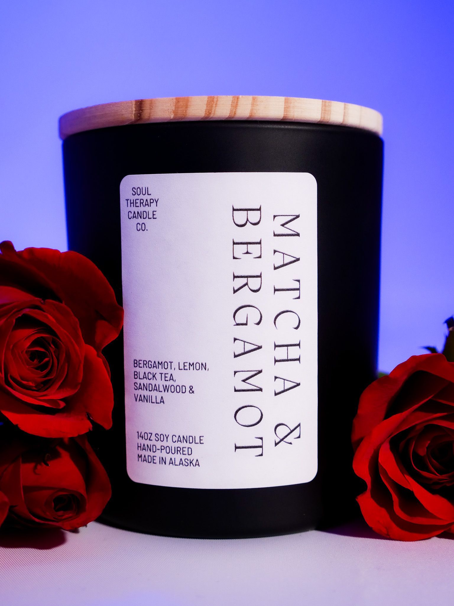 A matcha and bergamot candle is surrounded by red roses
