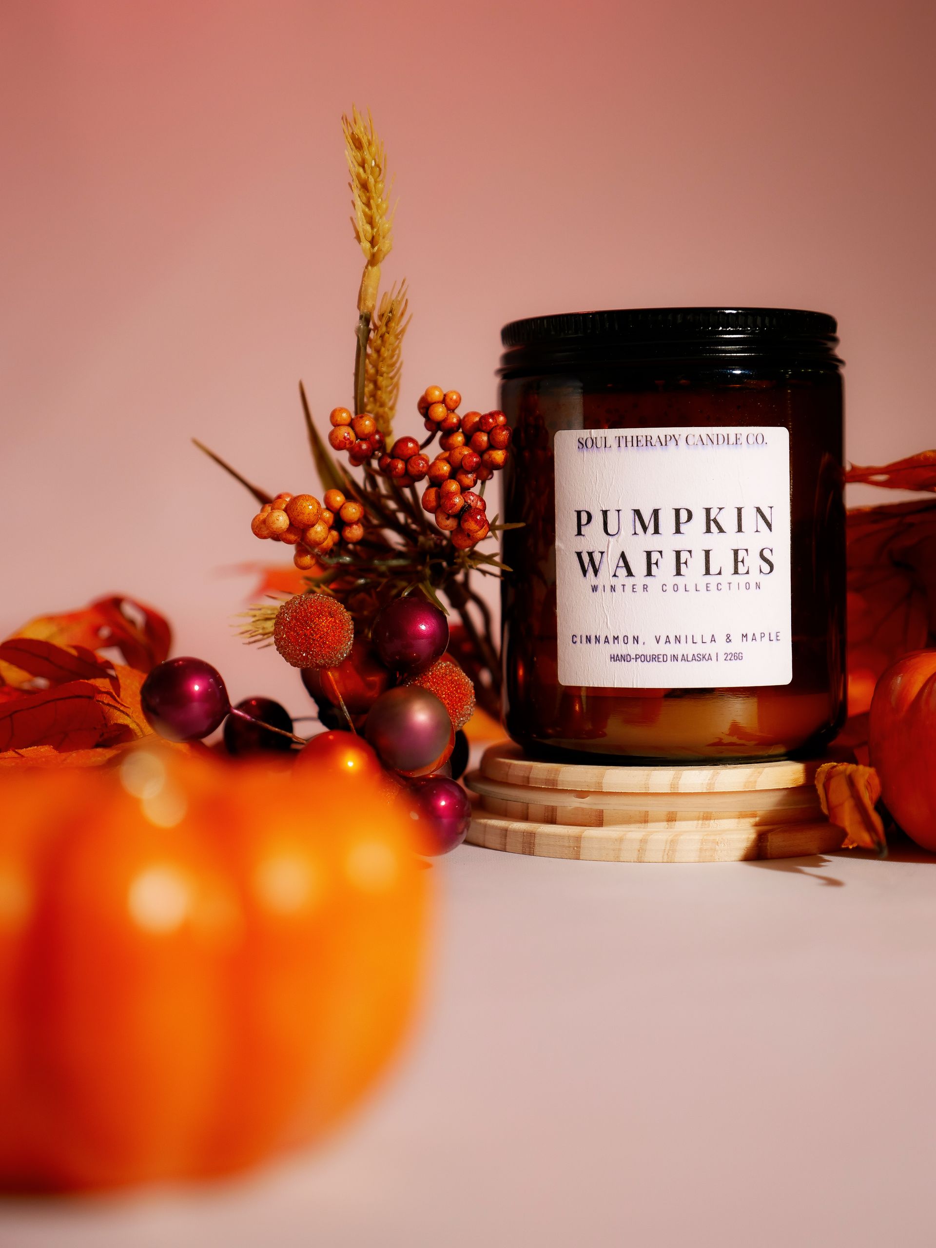 A jar of pumpkin waffles candle is sitting on a table next to pumpkins.