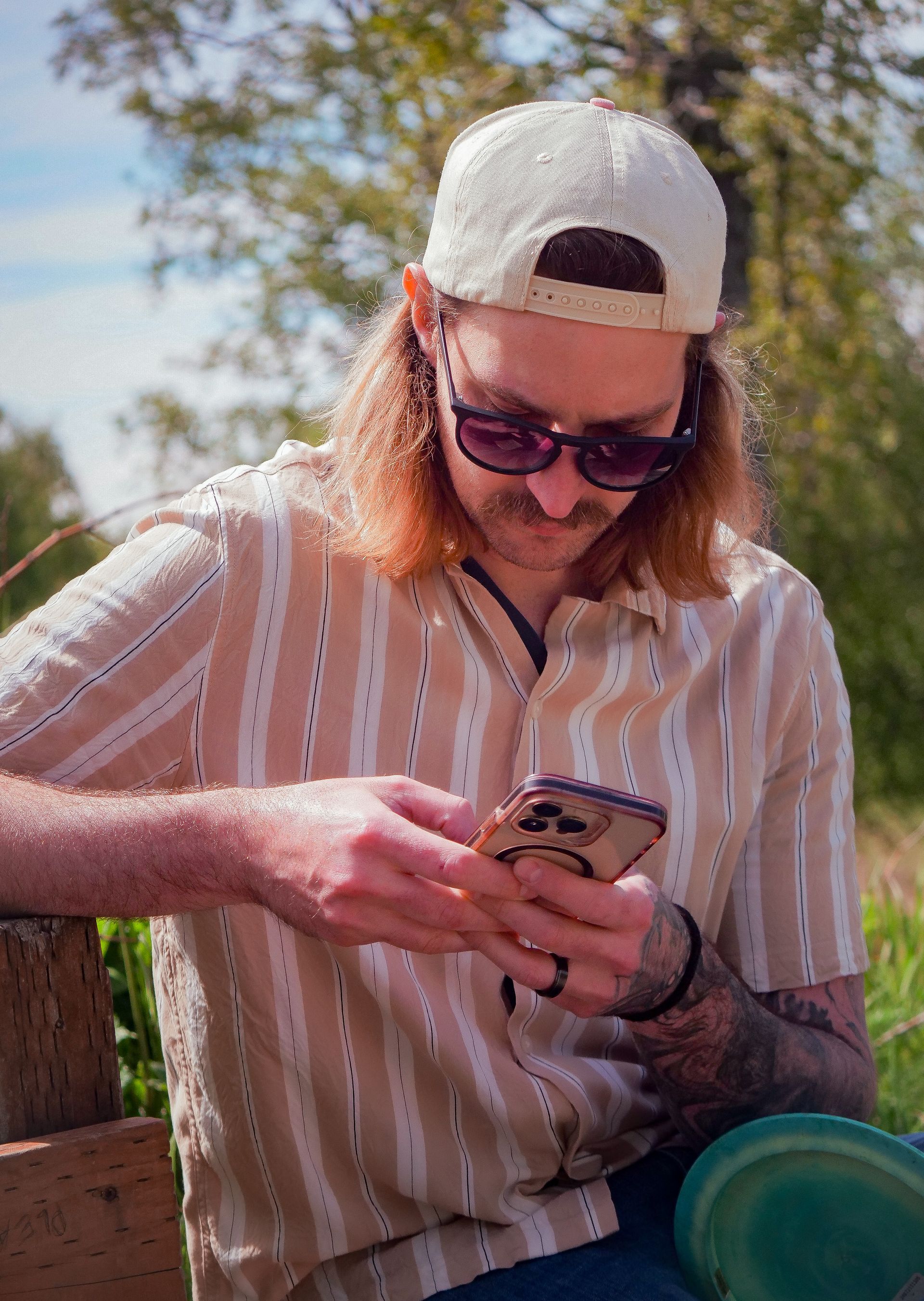 A man wearing sunglasses and a baseball cap is looking at his cell phone.
