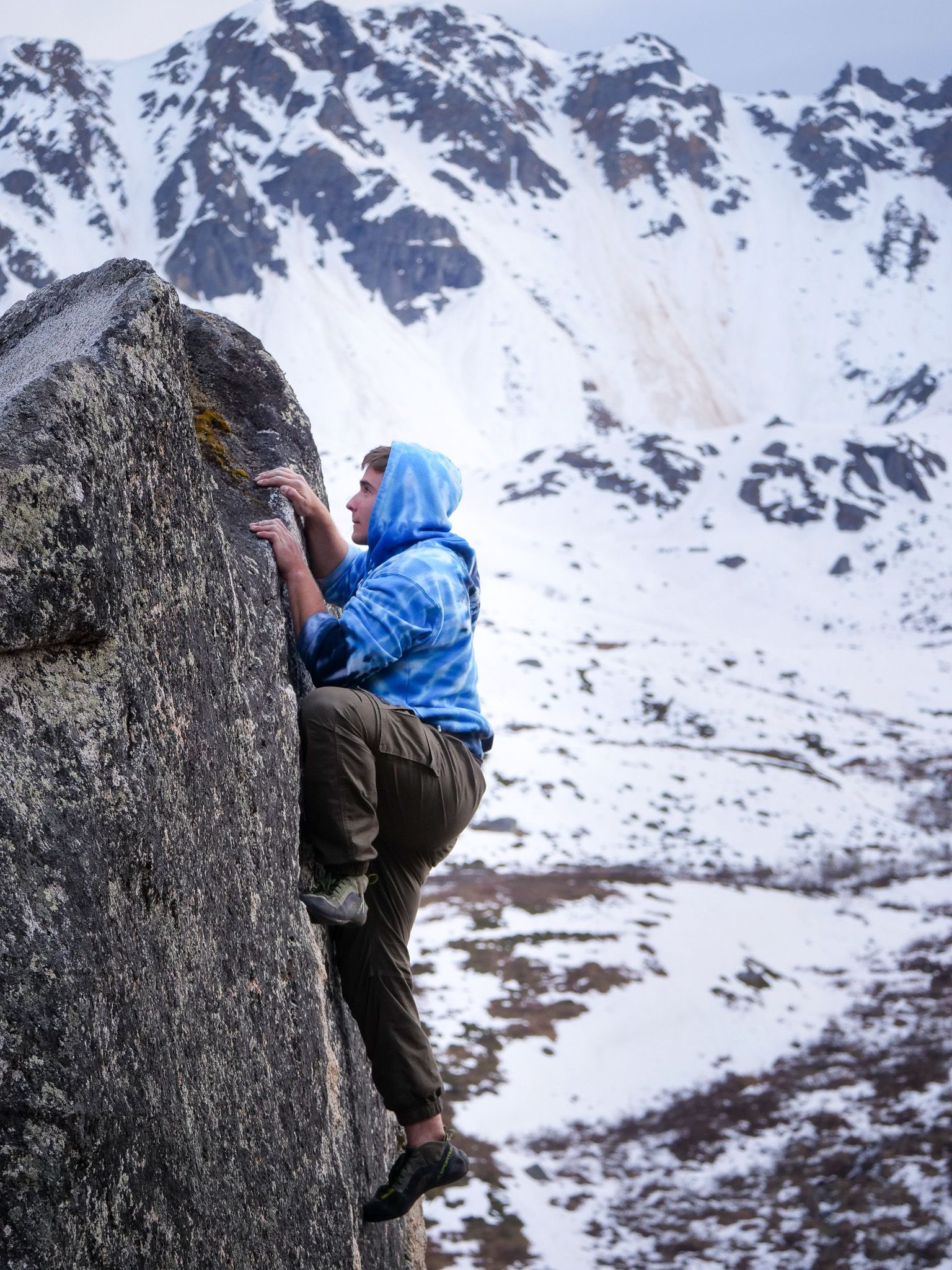 A man in a blue jacket is climbing a rock in the mountains.