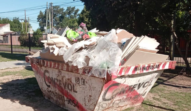 Contenedor de basura desbordado de escombros de construcción en una soleada calle residencial.