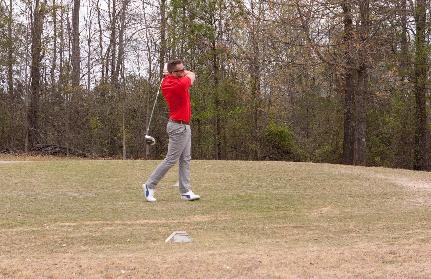 A man in a red shirt is swinging a golf club on a golf course.