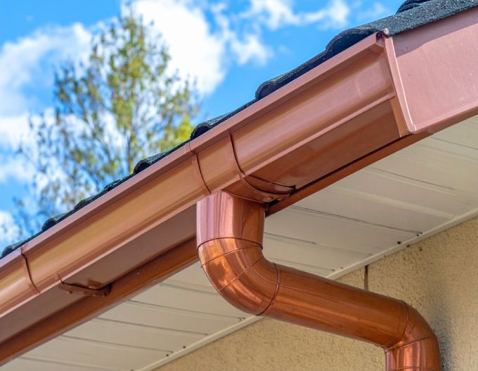 Copper rain gutter on a house with a blue sky background.