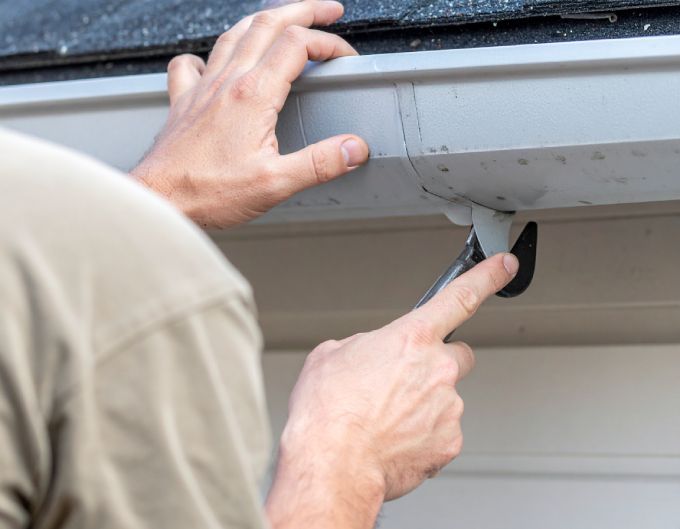 Person installing or repairing a gutter on a house, using a tool.
