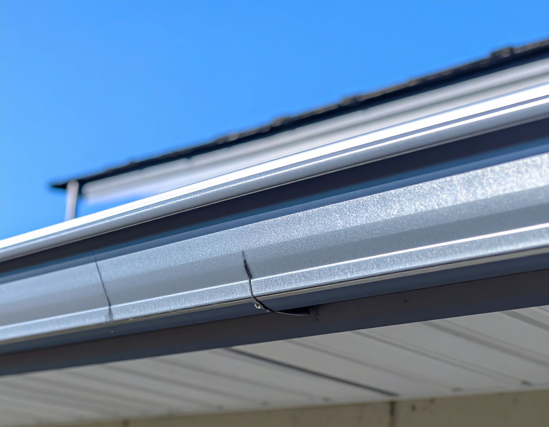 Close-up of gray metal roof gutter and soffit against a blue sky