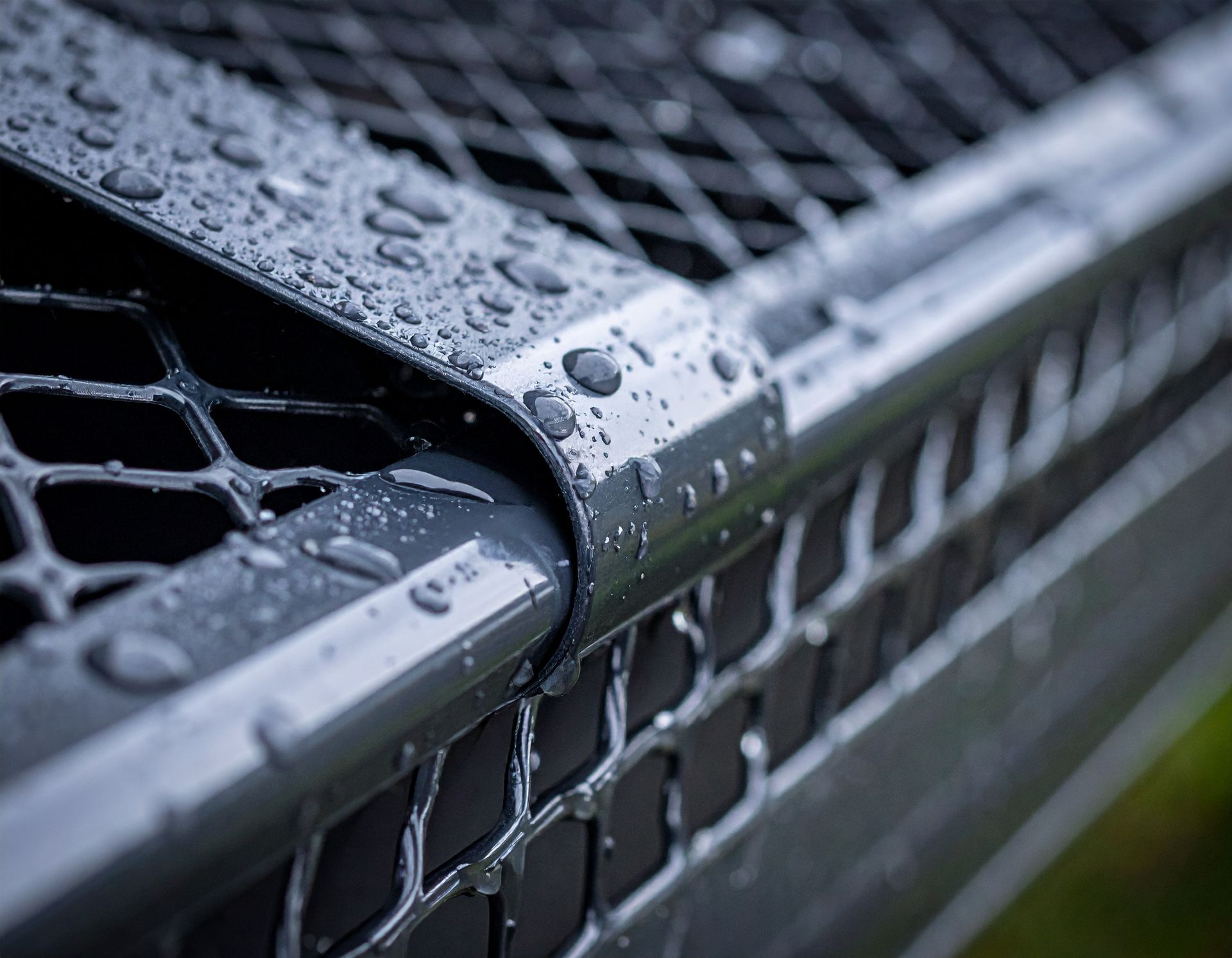 Close-up of a wet black metal fence with water droplets and blurred background