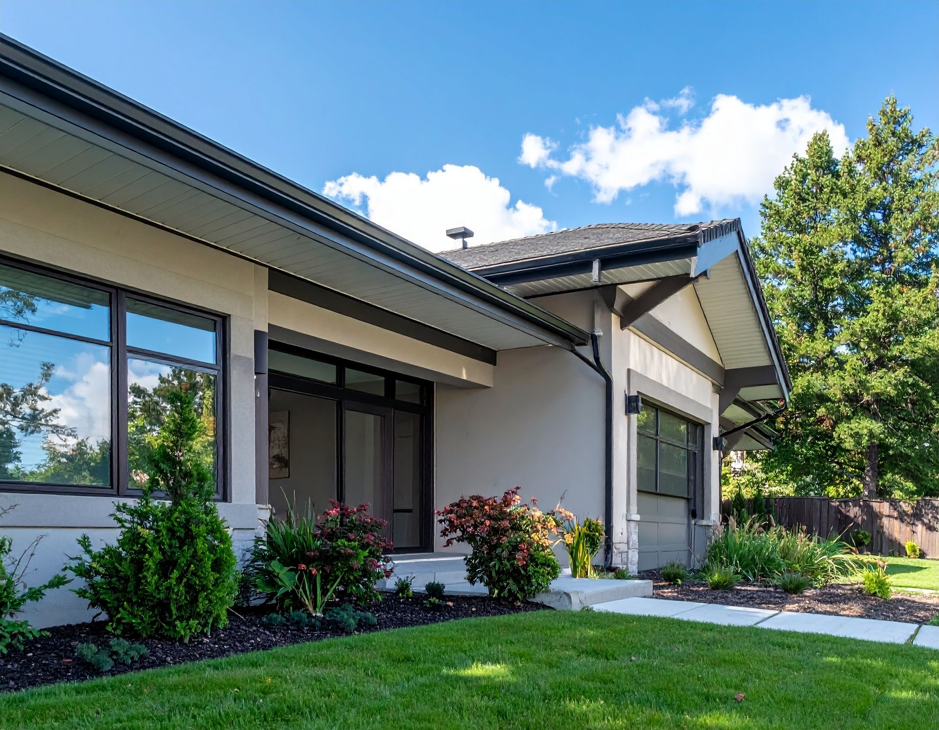 Modern single-story house exterior with a green lawn, shrubs, and blue sky