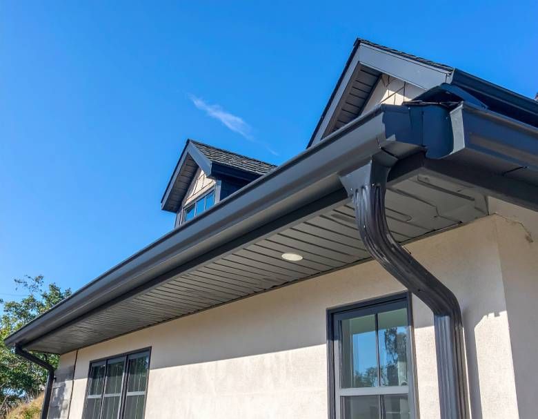 Black rain gutters and downspout on a house with a blue sky background.