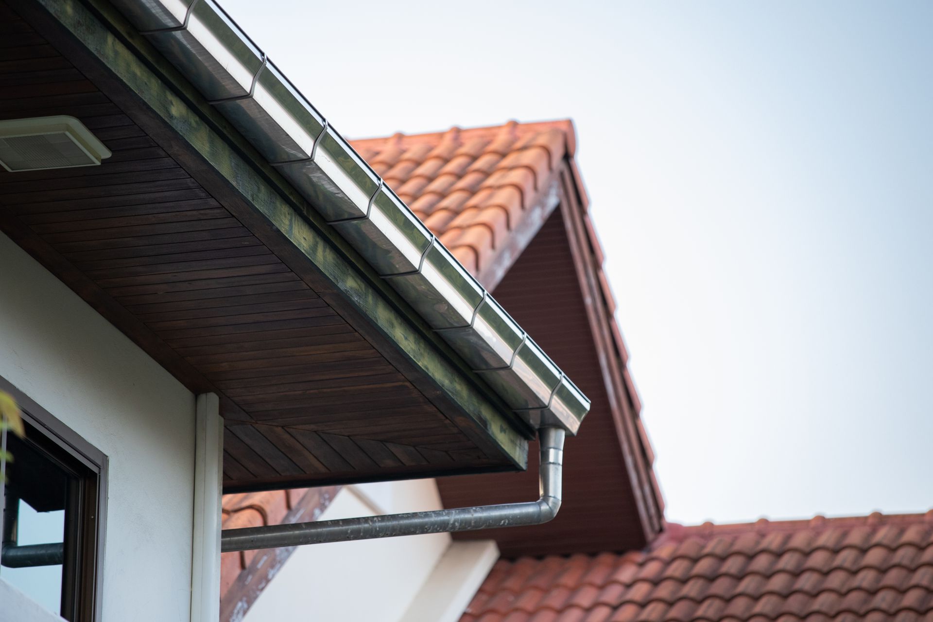 Guttering on a house with a red-tiled roof, brown eaves, and white siding.